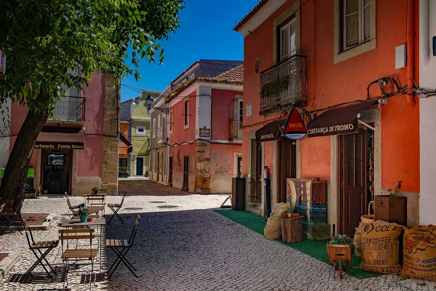 Cobblestone street in Setubal's old town, lined with colorful buildings, quaint cafes, and hanging decorations, creating a vibrant and inviting atmosphere.